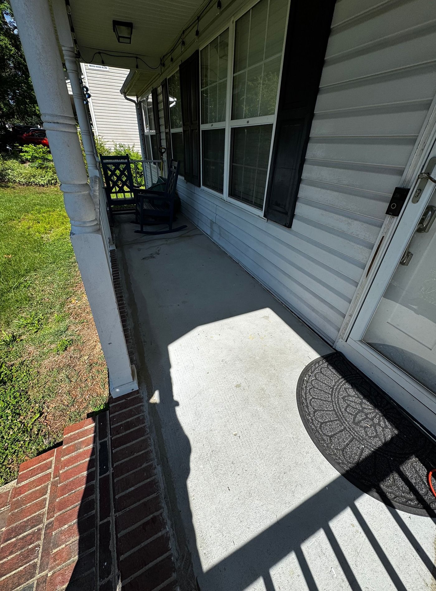 Front porch with white siding, screened windows, brick edge, and black metal railing in sunlight