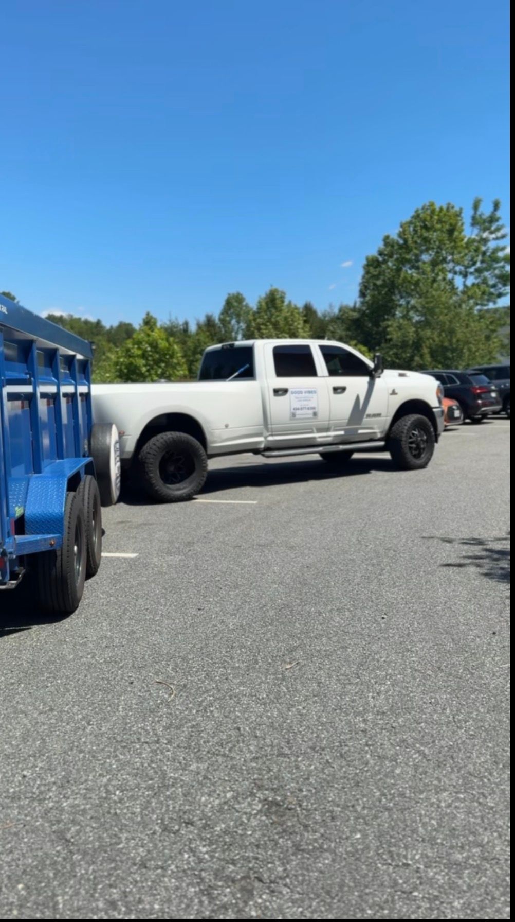 White lifted pickup truck parked in a lot beside a blue truck under a clear blue sky