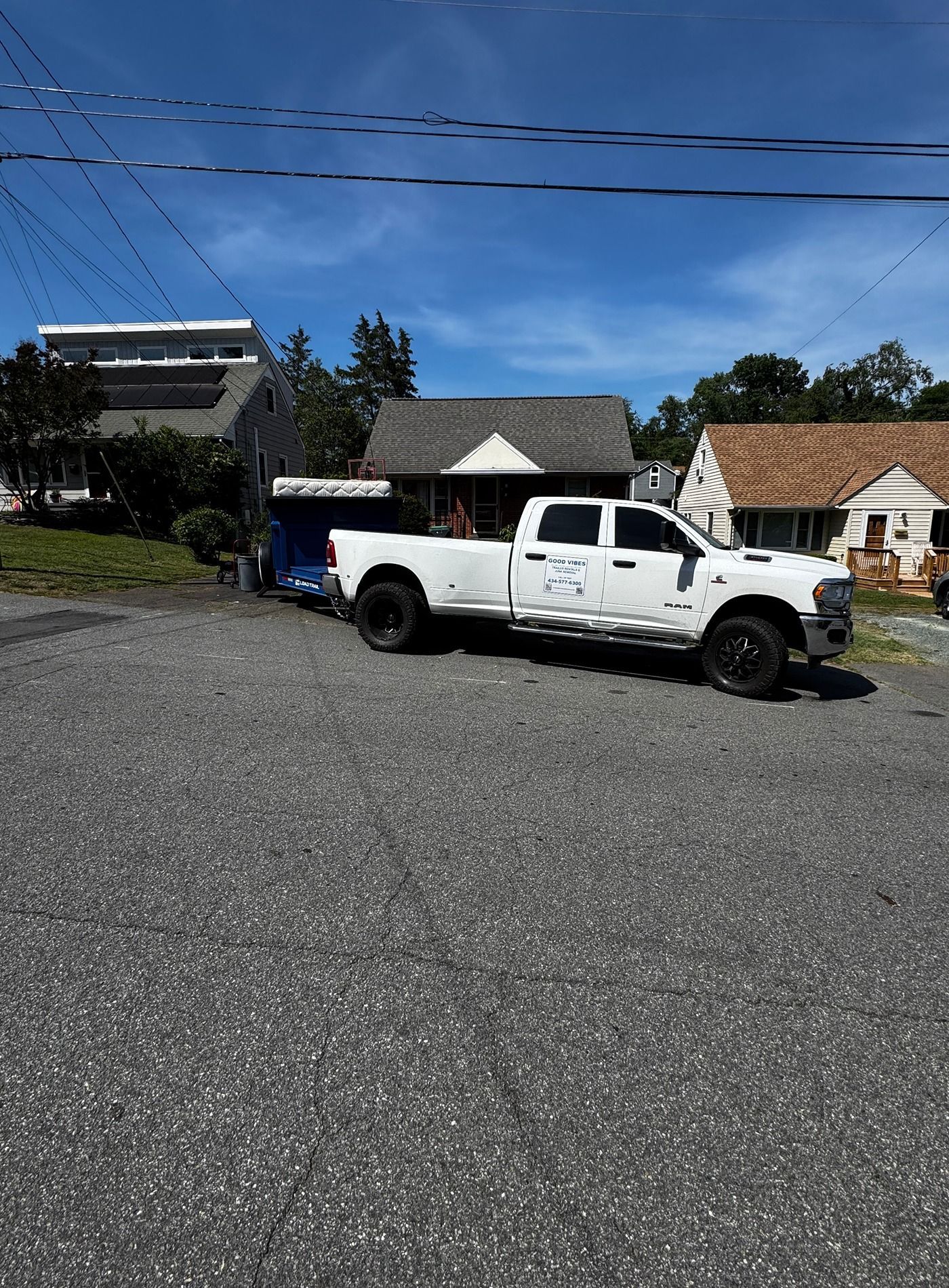 White pickup truck with a blue trailer parked on a gravel lot near houses under a clear blue sky