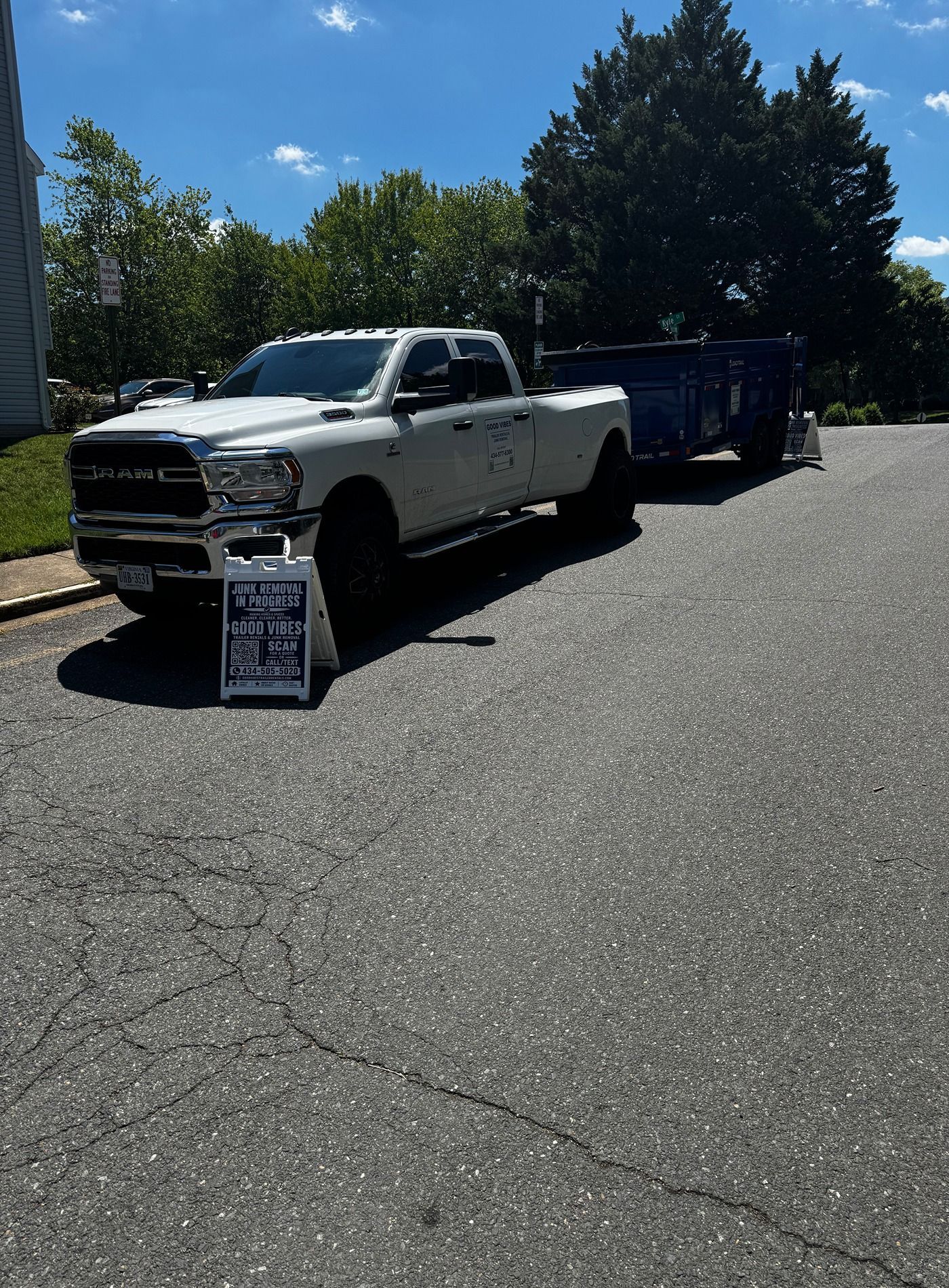White pickup truck with a trailer parked in a lot beside a roadside sign on a sunny day