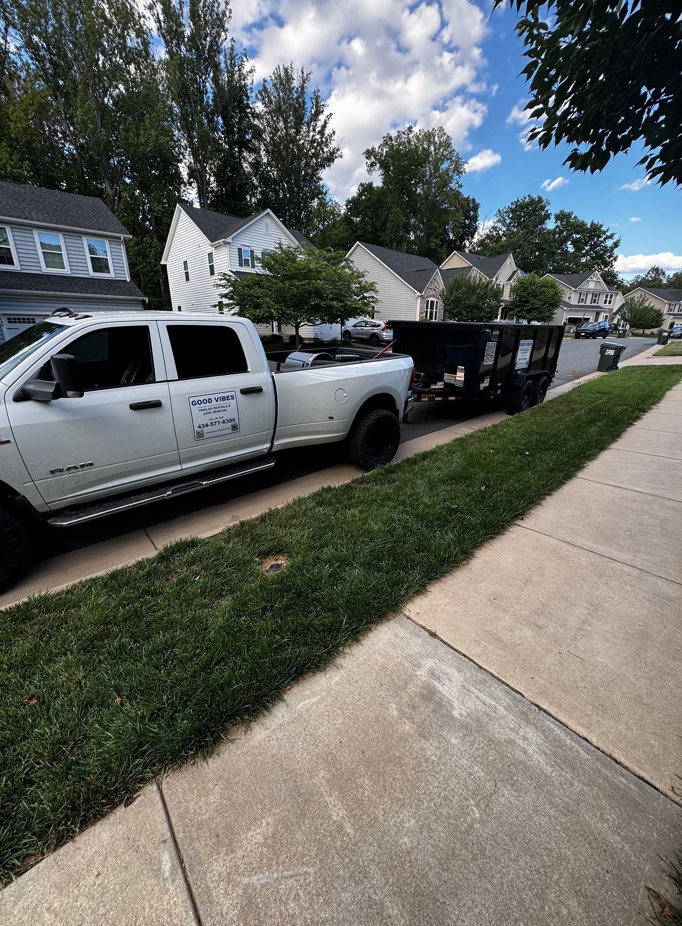 White pickup truck with a black trailer parked along a suburban sidewalk, near houses and trees