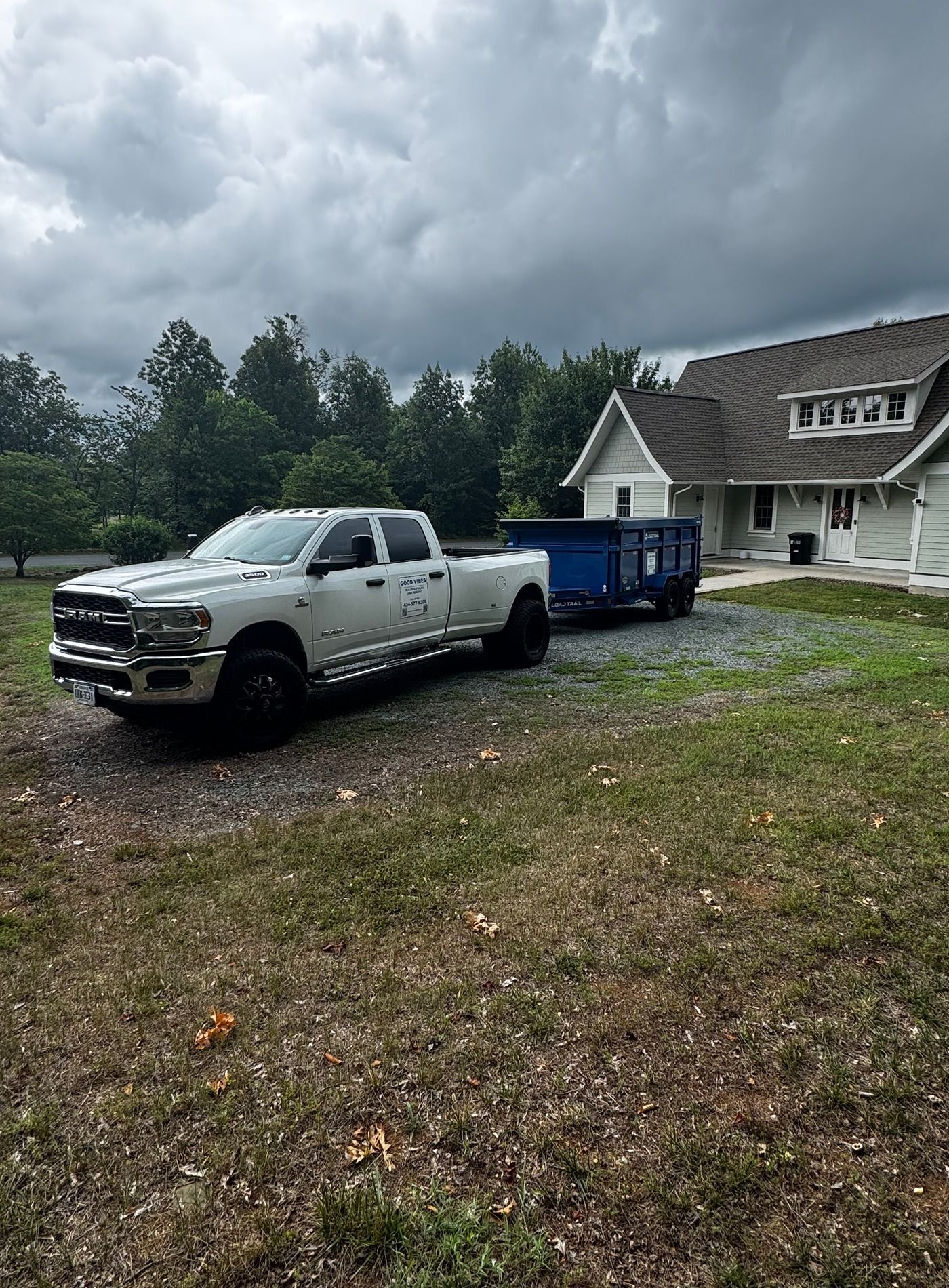 White pickup truck parked beside a blue dumpster and house under dark storm clouds.