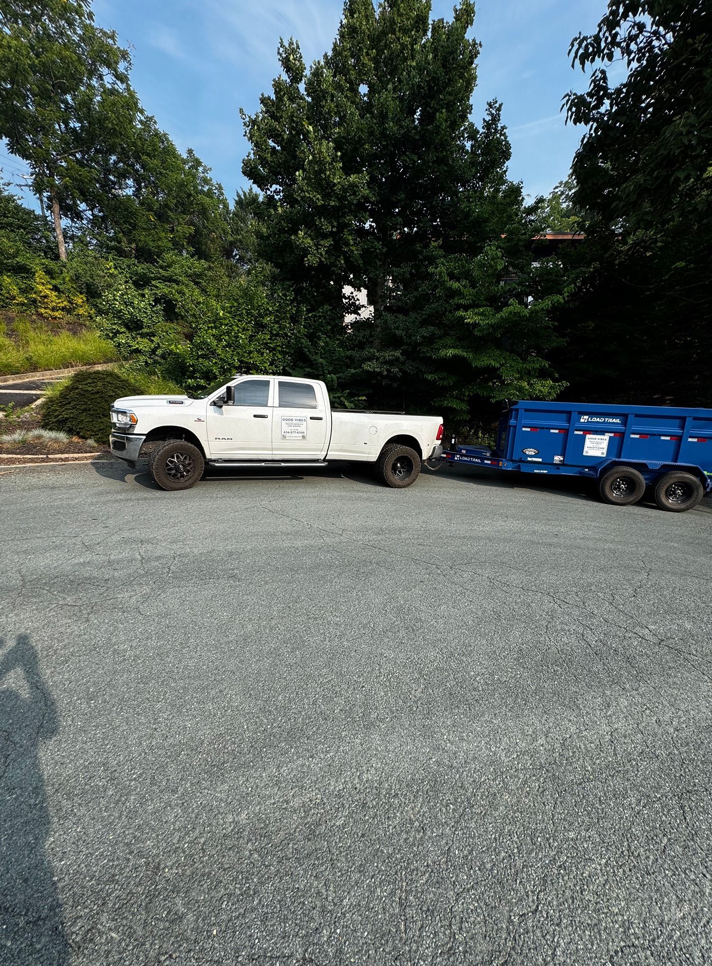 White pickup truck towing a blue trailer on a gravel lot with trees in the background