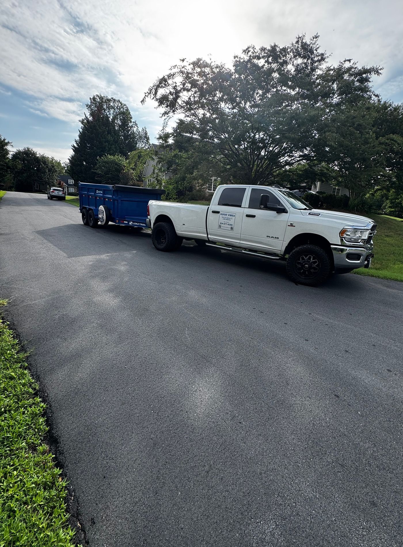 White pickup truck towing a blue trailer on a quiet residential street under cloudy skies