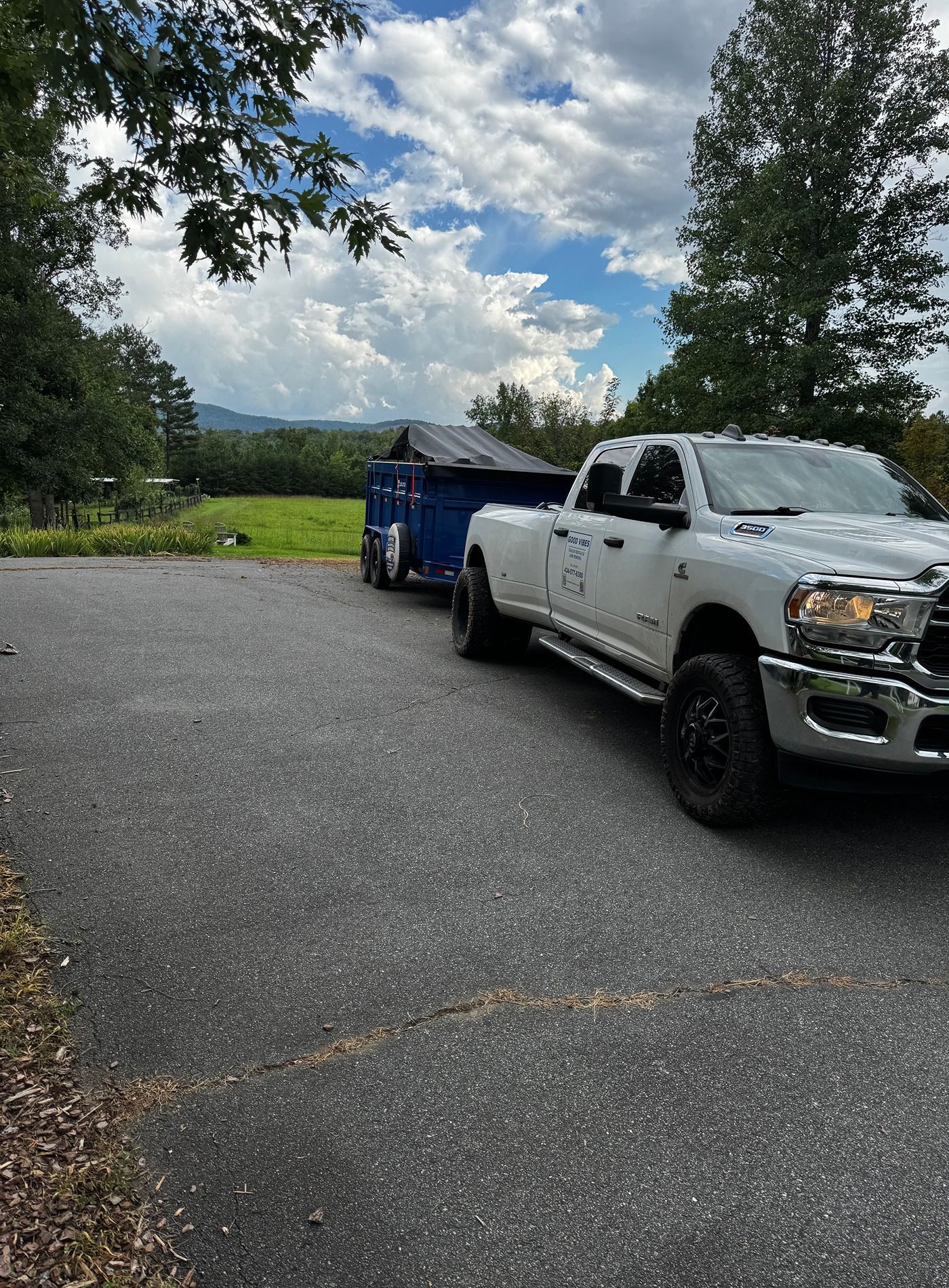 White pickup truck parked on a paved lot beside a blue trailer under a cloudy sky.