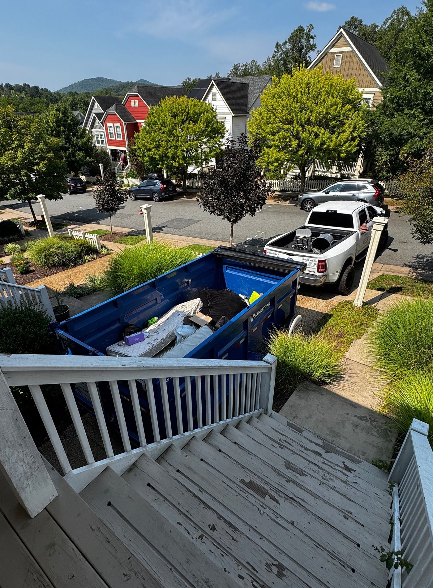 View from porch stairs of a street with a blue dumpster and a white pickup truck in a suburban neighborhood
