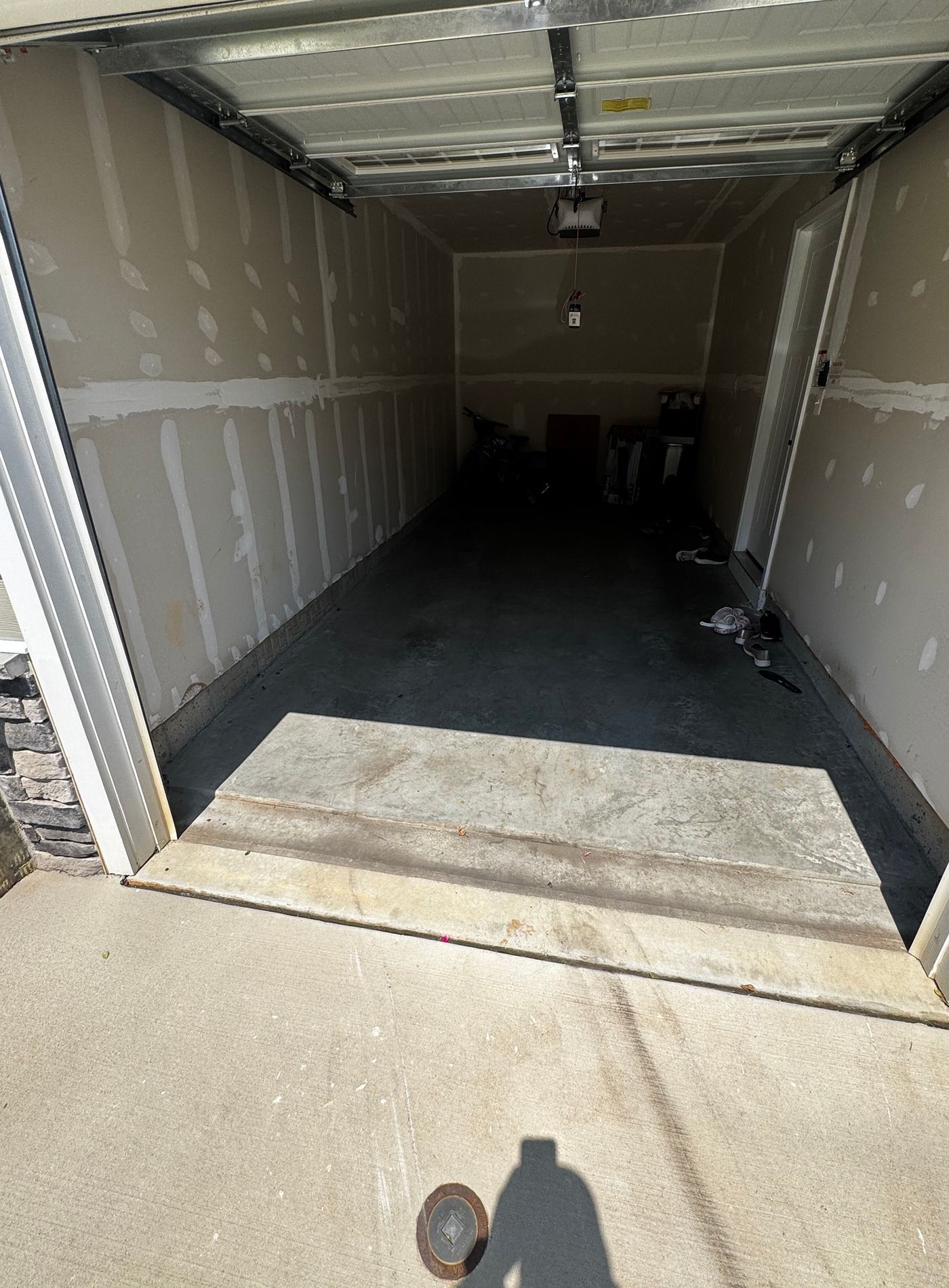 Open garage with a concrete floor and drywall walls, viewed from the driveway.