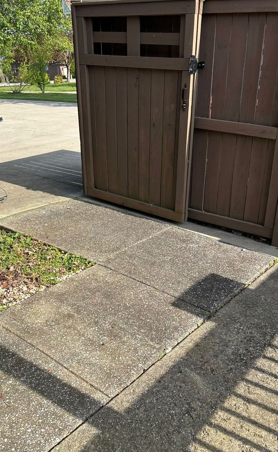 A wooden trash can is sitting on the sidewalk next to a wooden fence.