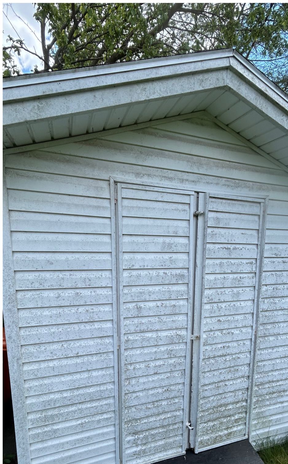 A white shed with a roof and shutters on the doors.