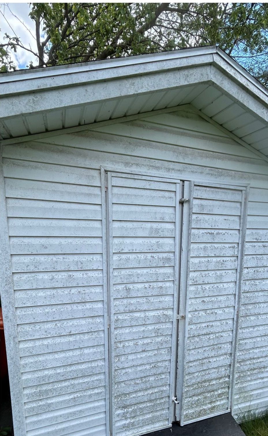 A white shed with a roof and shutters on the doors.