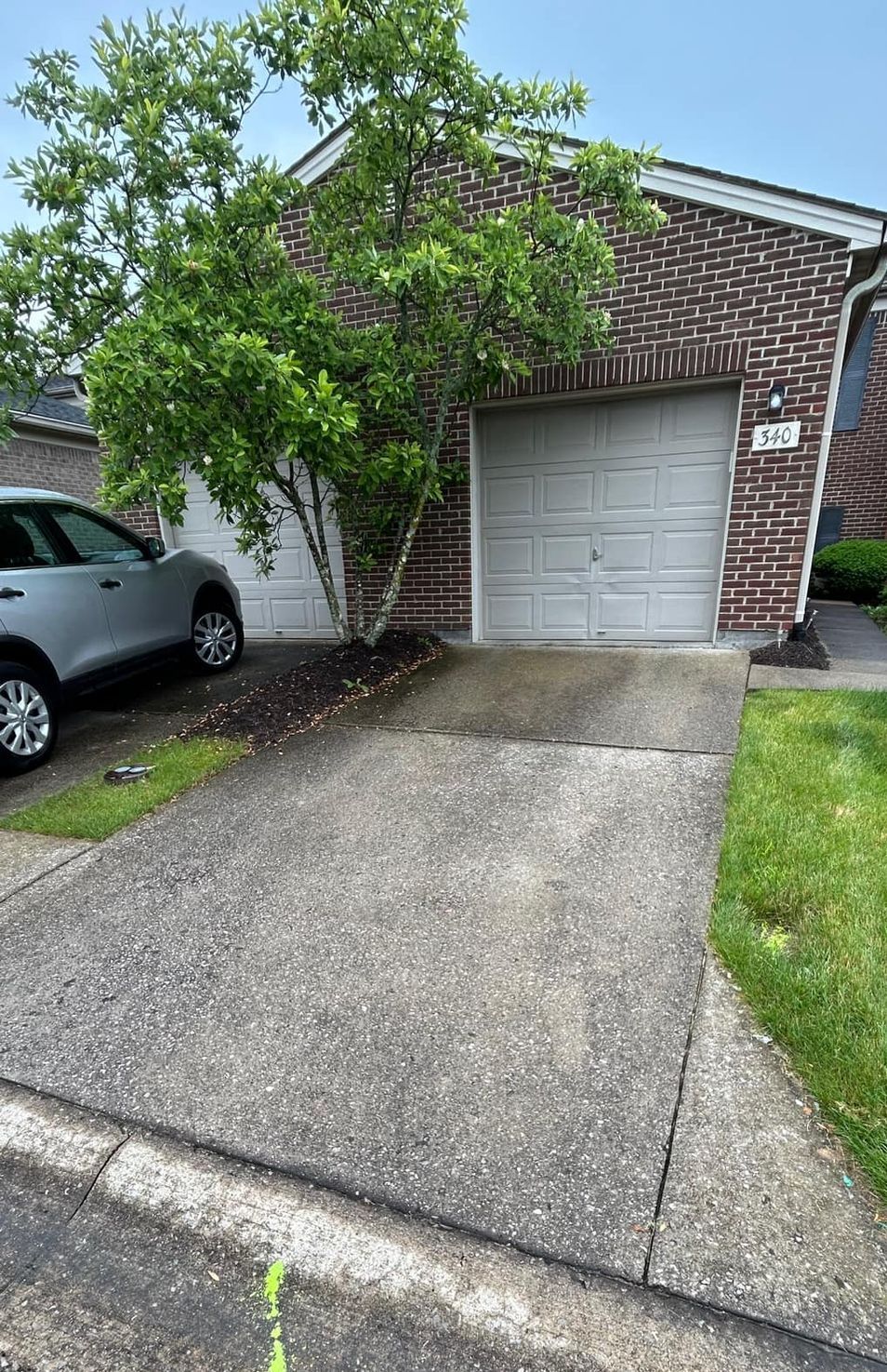 A car is parked in front of a brick house with a garage.