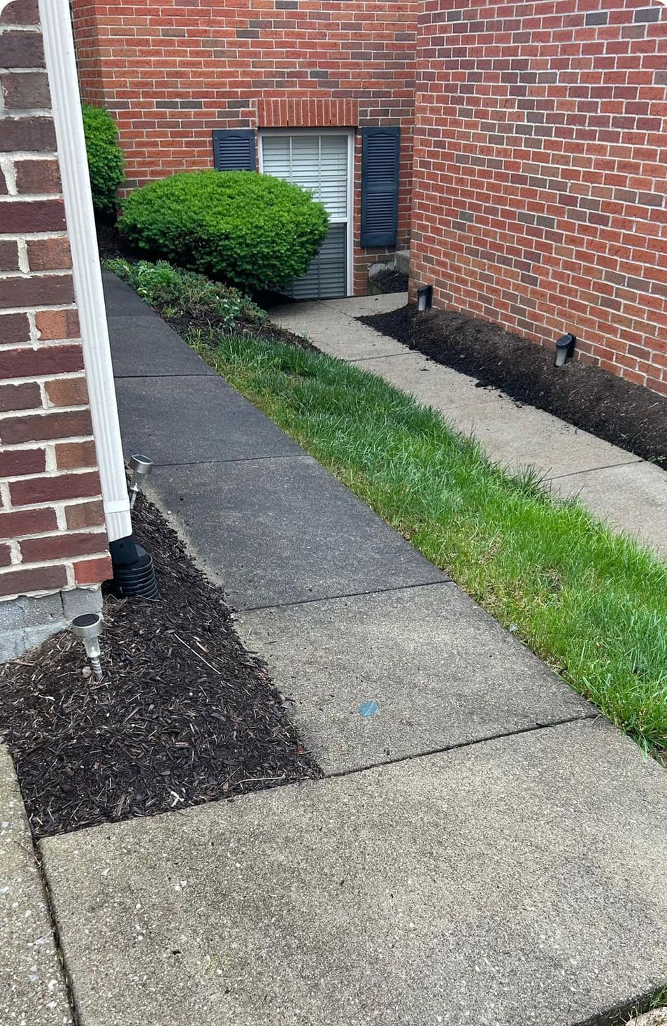 A sidewalk leading to a brick building with a garage door.