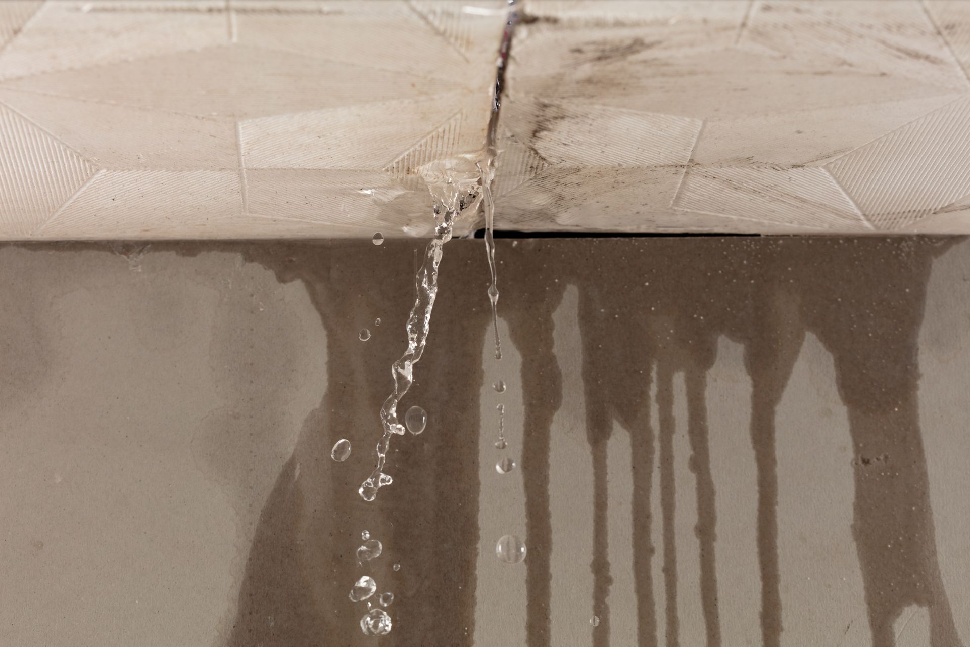 Water leaking from a cracked ceiling tile, dripping down a wall.