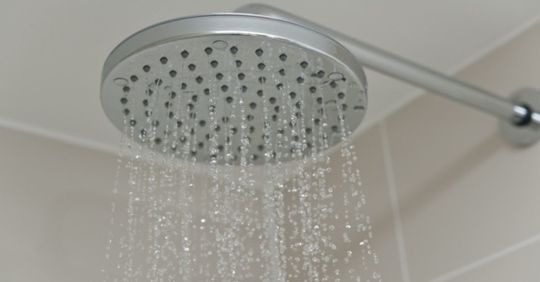 Showerhead with water spraying downwards, set against white tiles.