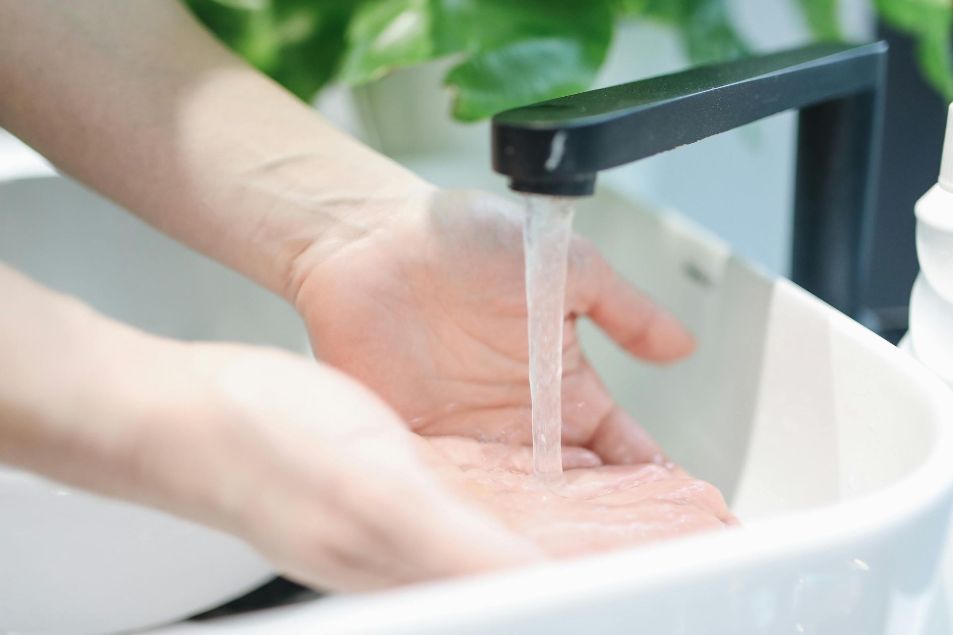 Person washing hands under a modern black faucet in a white sink.