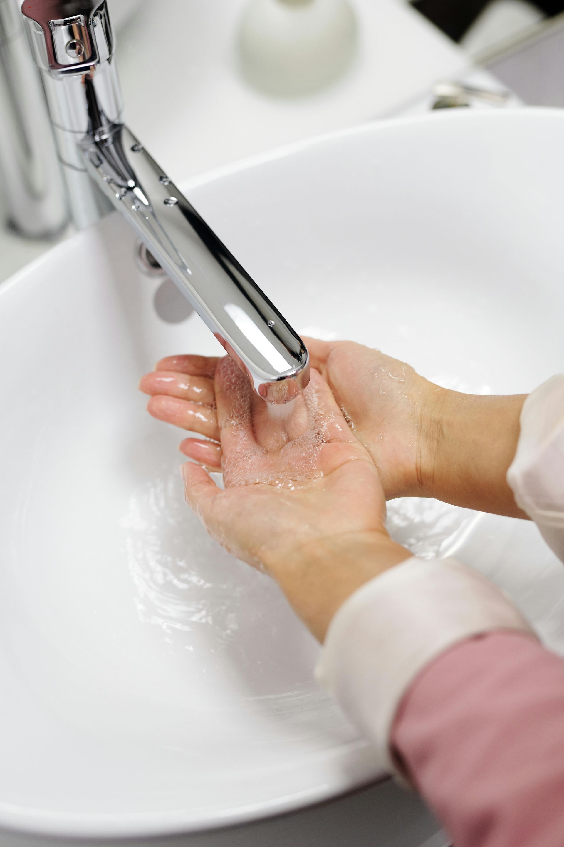 Hands being washed under a chrome faucet in a white sink.