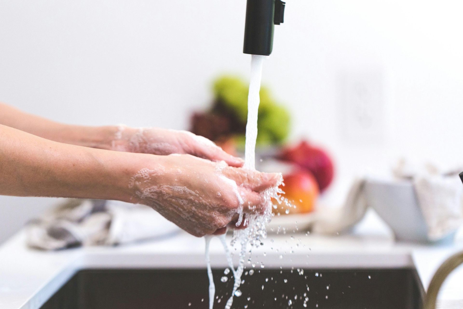 Hands washing under a running faucet in a kitchen sink.