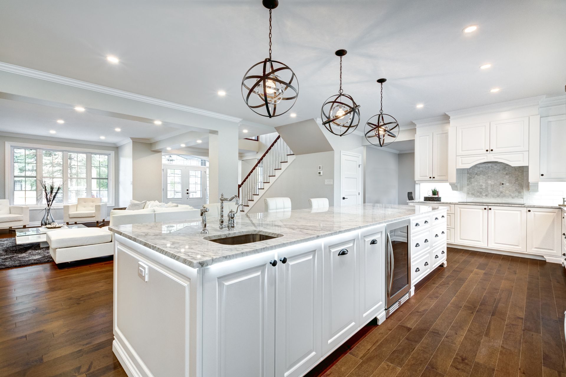 Spacious white kitchen with dark wood floors, island with sink, and three pendant lights.