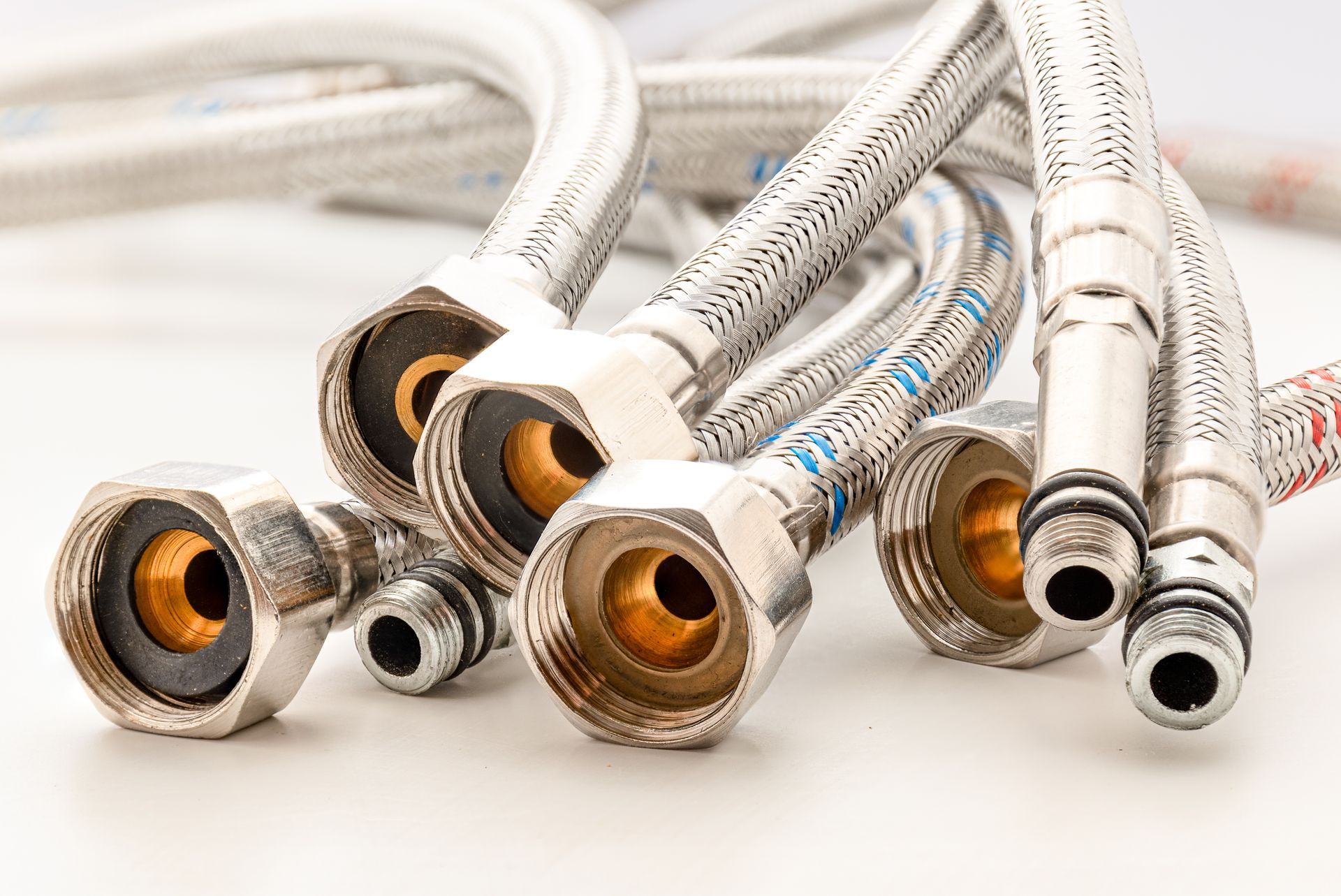 Braided stainless steel plumbing hoses with brass fittings, laying on a white surface.