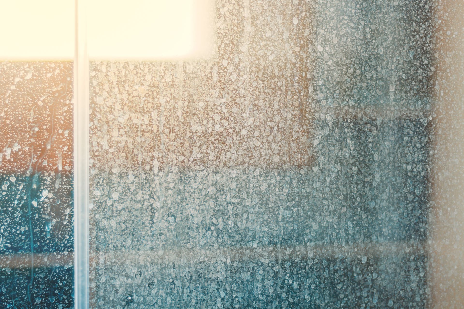 Shower glass covered in hard water stains, with a window frame visible on the left.