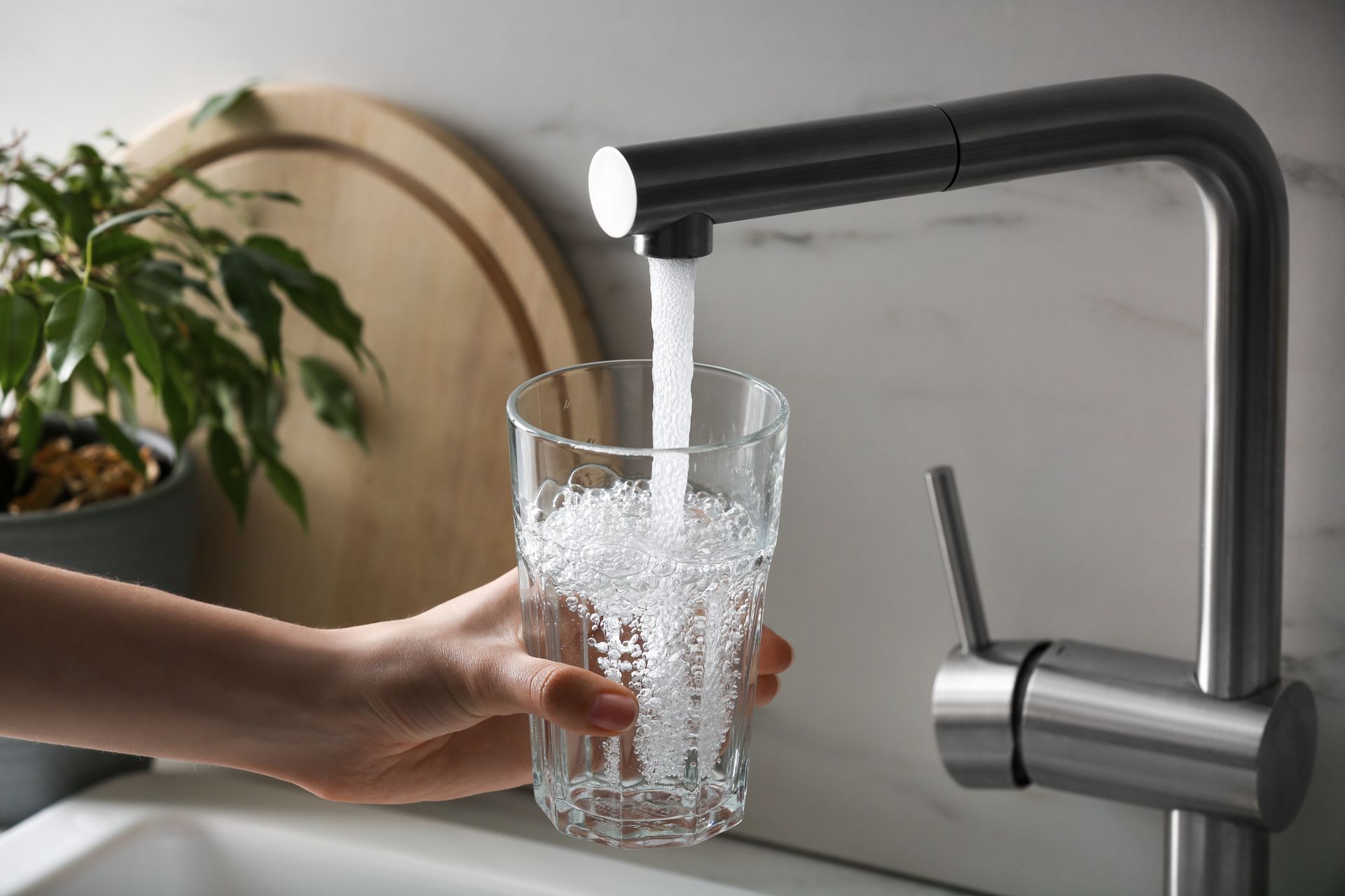 A person filling a clear glass with water from a modern chrome faucet in a kitchen.