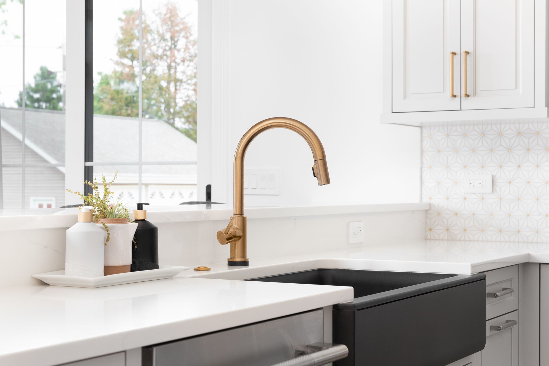 Gold faucet over black sink in a bright kitchen with white cabinets and countertop by a window.