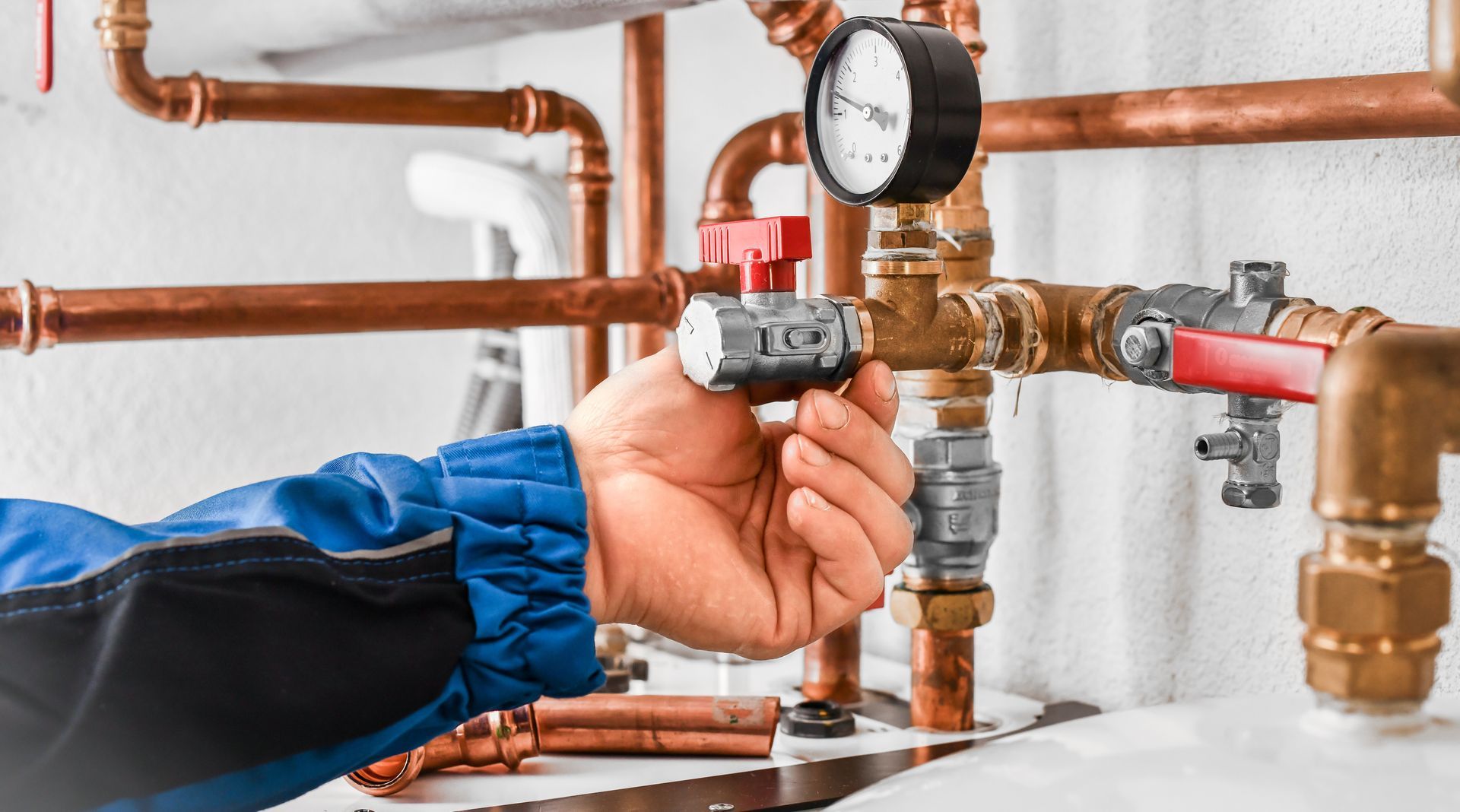Hand adjusting a valve on copper pipes with gauges, in a mechanical room.