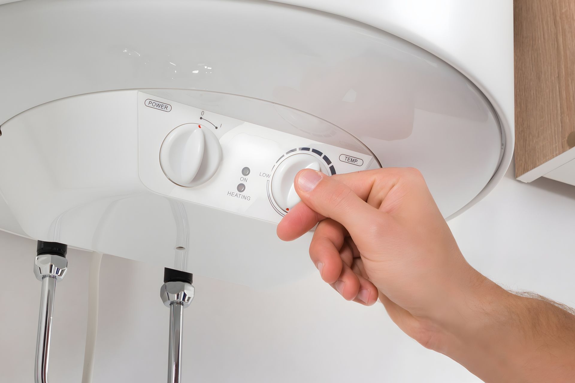 Person's hand turning a dial on a white water heater, likely adjusting the temperature.