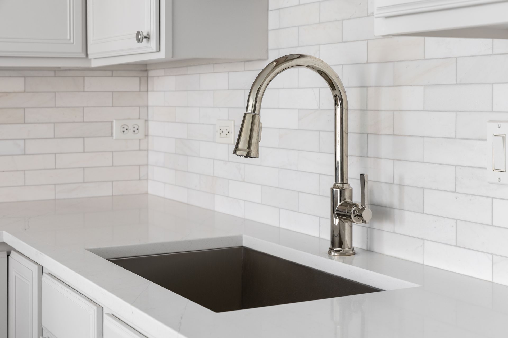Stainless steel kitchen faucet over a gray rectangular sink on a white countertop with white subway tile backsplash.
