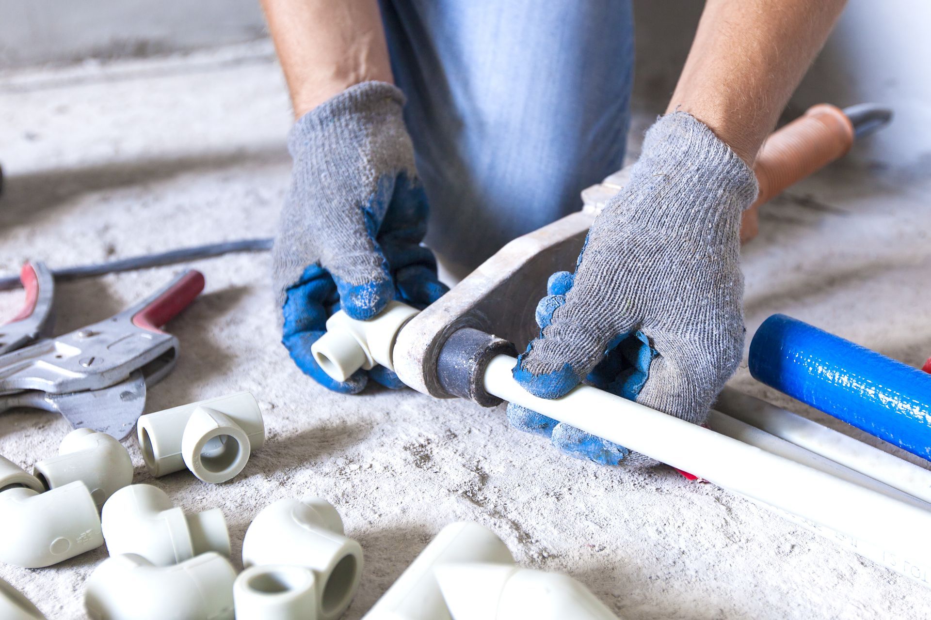 Hands in gloves assembling white PVC plumbing parts on a concrete floor.