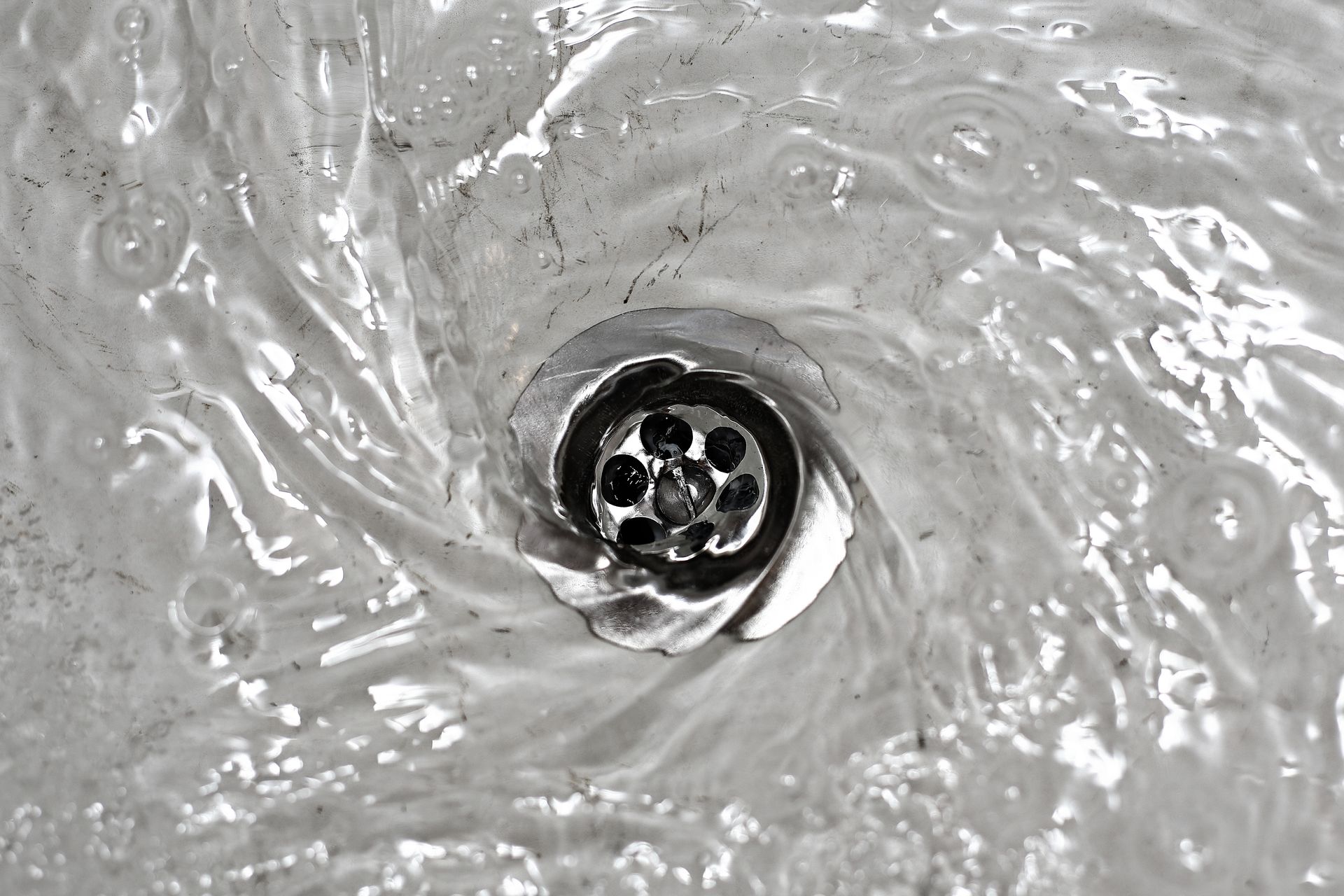 Water swirling down a drain in a sink, creating a vortex effect.