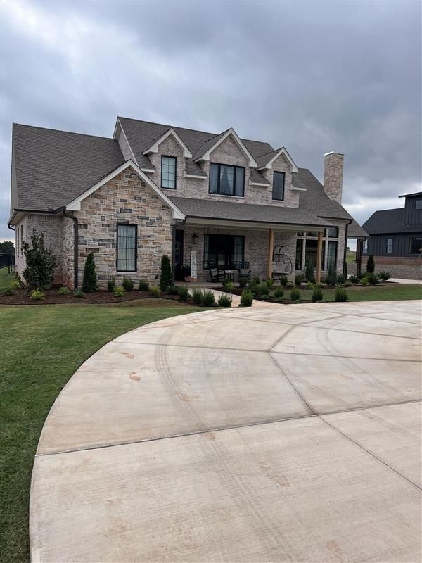 A large, modern brick house with a curved driveway under a cloudy sky.