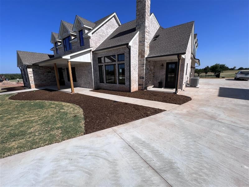 Two-story brick house with dark roof and large windows; a concrete driveway and landscaped yard.