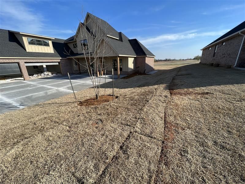 New home with bare trees, dry grass, and a paved driveway under a bright blue sky.