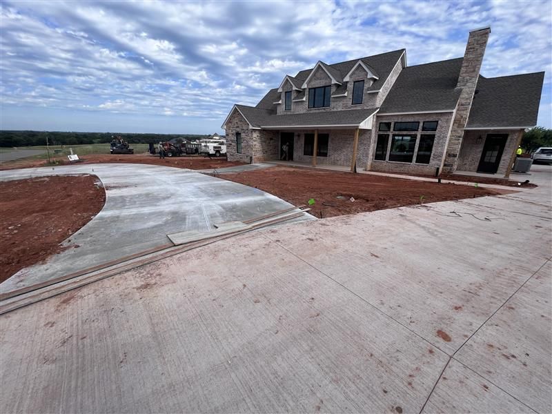 New house with stone facade, gray roof, and concrete driveway under a cloudy sky.