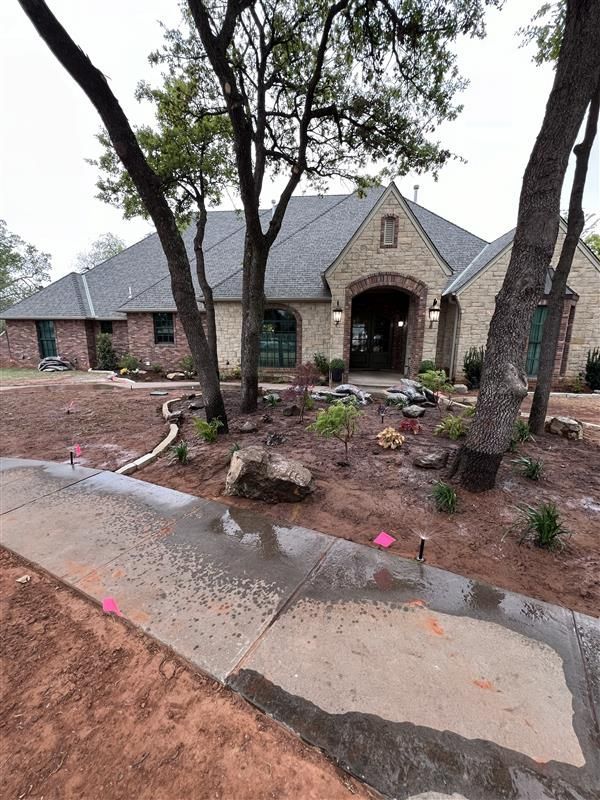 Stone house with brick accents, surrounded by newly landscaped yard and trees, with a sidewalk in front.