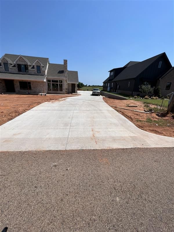 Newly poured concrete driveway between two houses under construction on a sunny day.