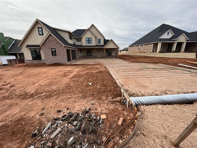 Construction site with two houses, one with brick and tan siding, the other with a dark roof.