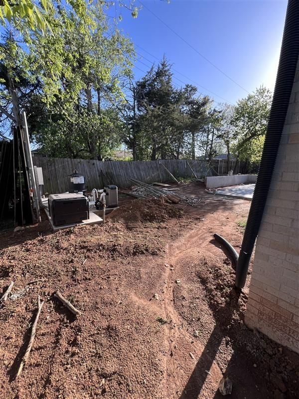 Backyard with dirt ground, a fence, and construction materials near a building.