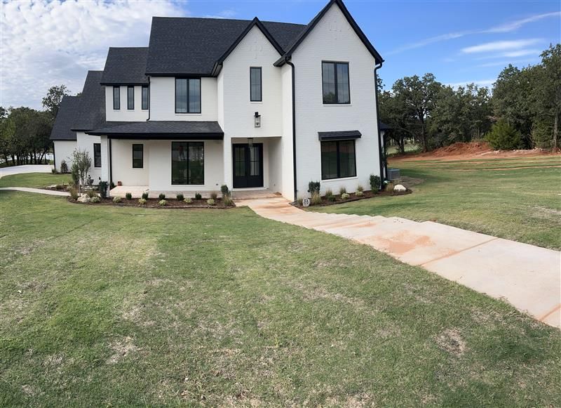 White two-story house with black trim, windows, and roof on a green lawn. Concrete path leads to front door.