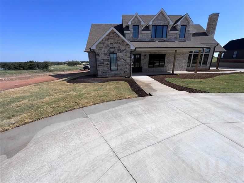 Stone-faced house with a long concrete driveway on a sunny day.