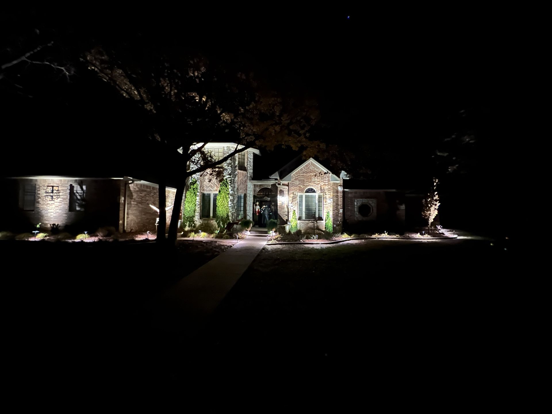 A house at night, illuminated by outdoor lights; a path leads to the front door.
