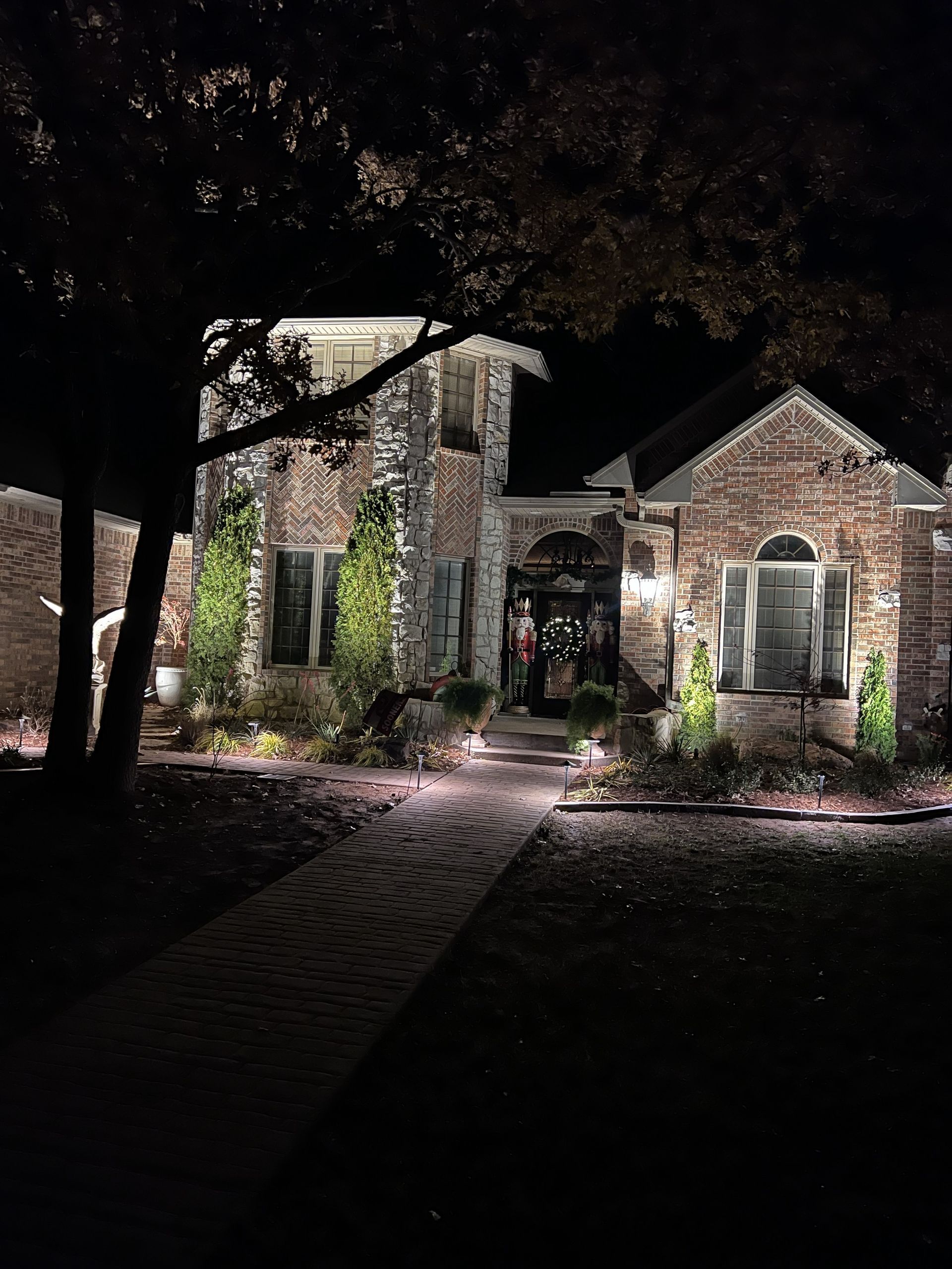 Night view of a brick house illuminated by outdoor lighting, with a brick path leading to the front door.