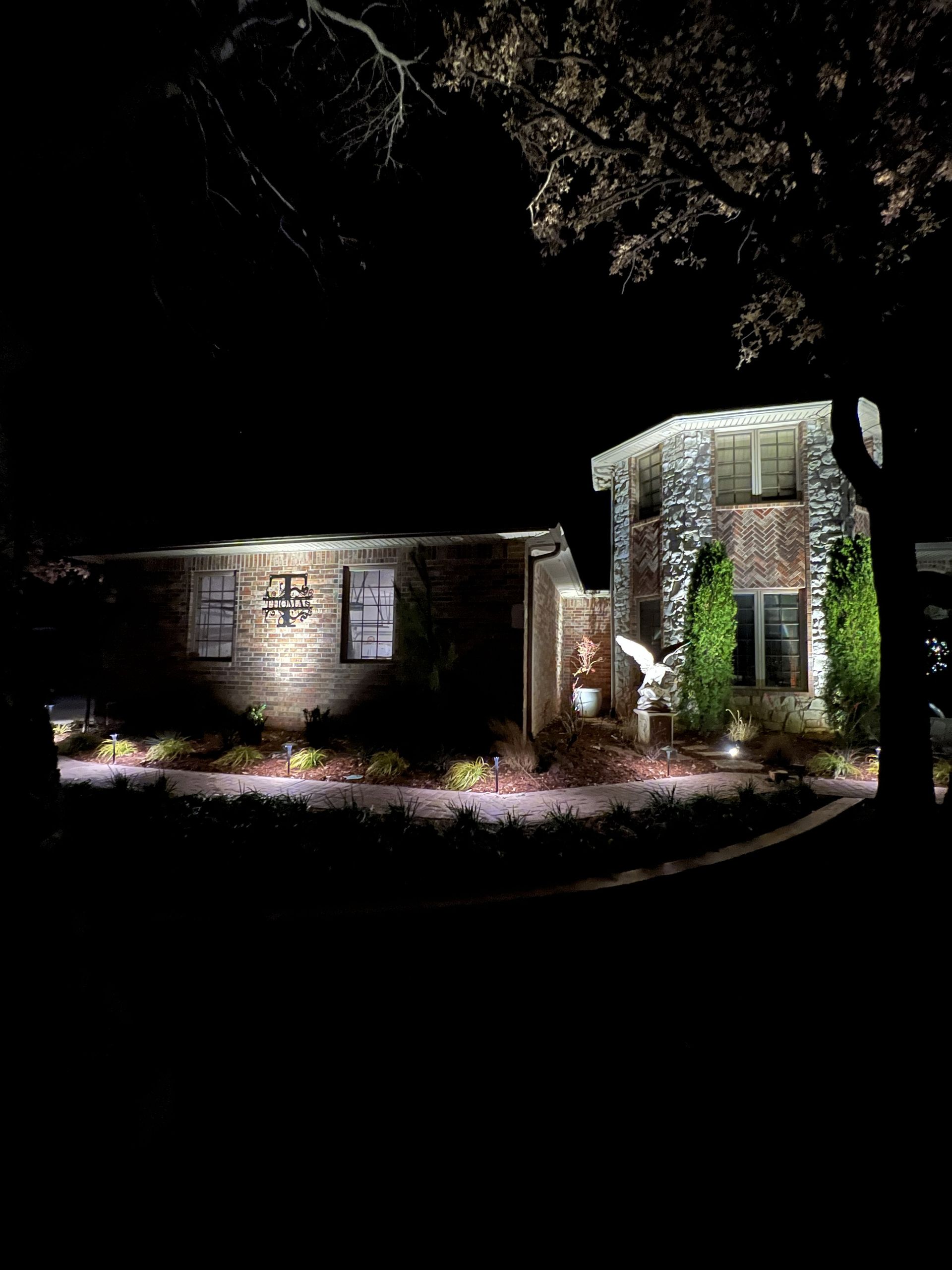 Night view of a stone house with illuminated facade and landscaping. Dark sky.