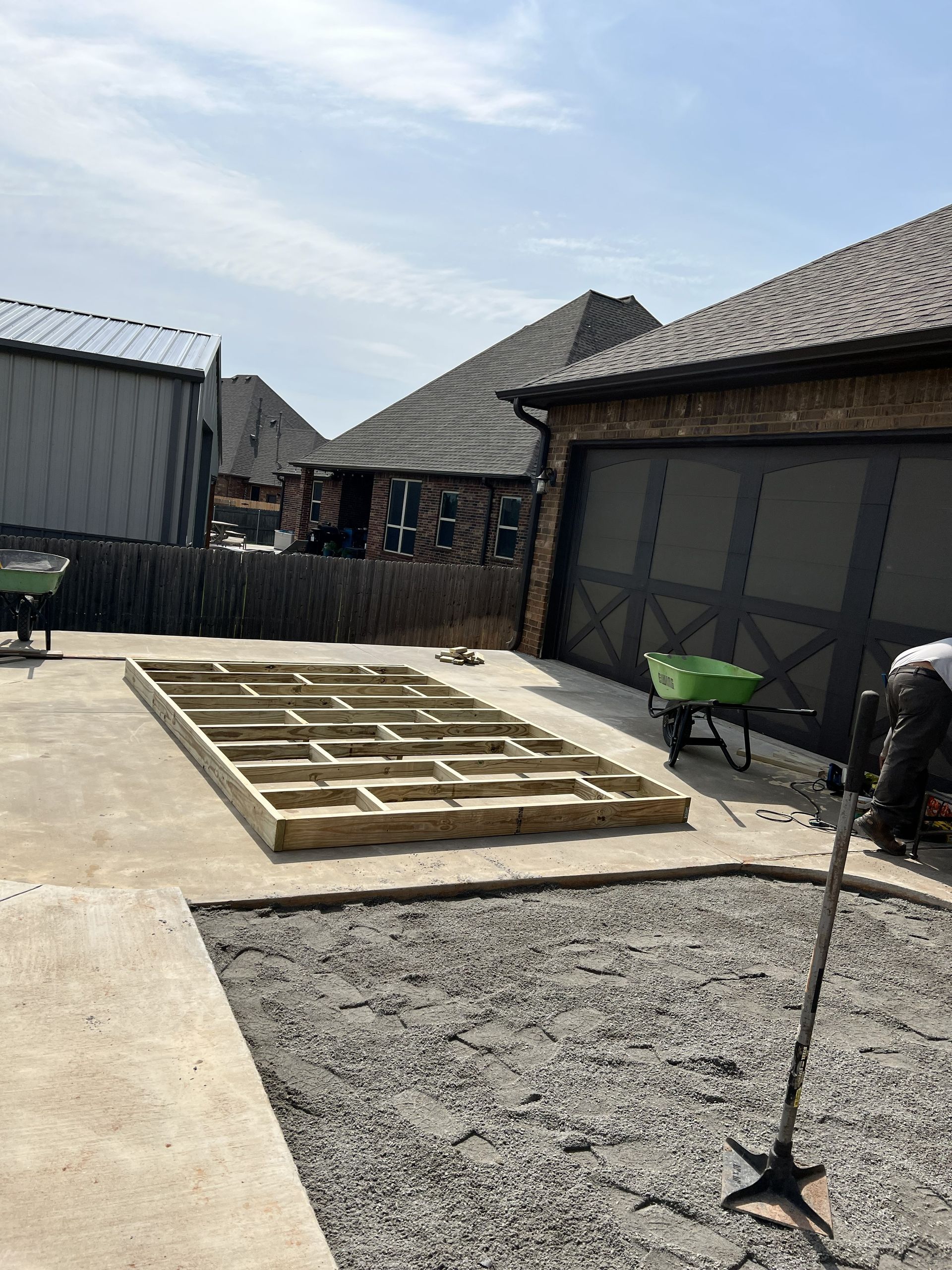 Wooden frame of a structure on a concrete surface, near a garage and gravel.