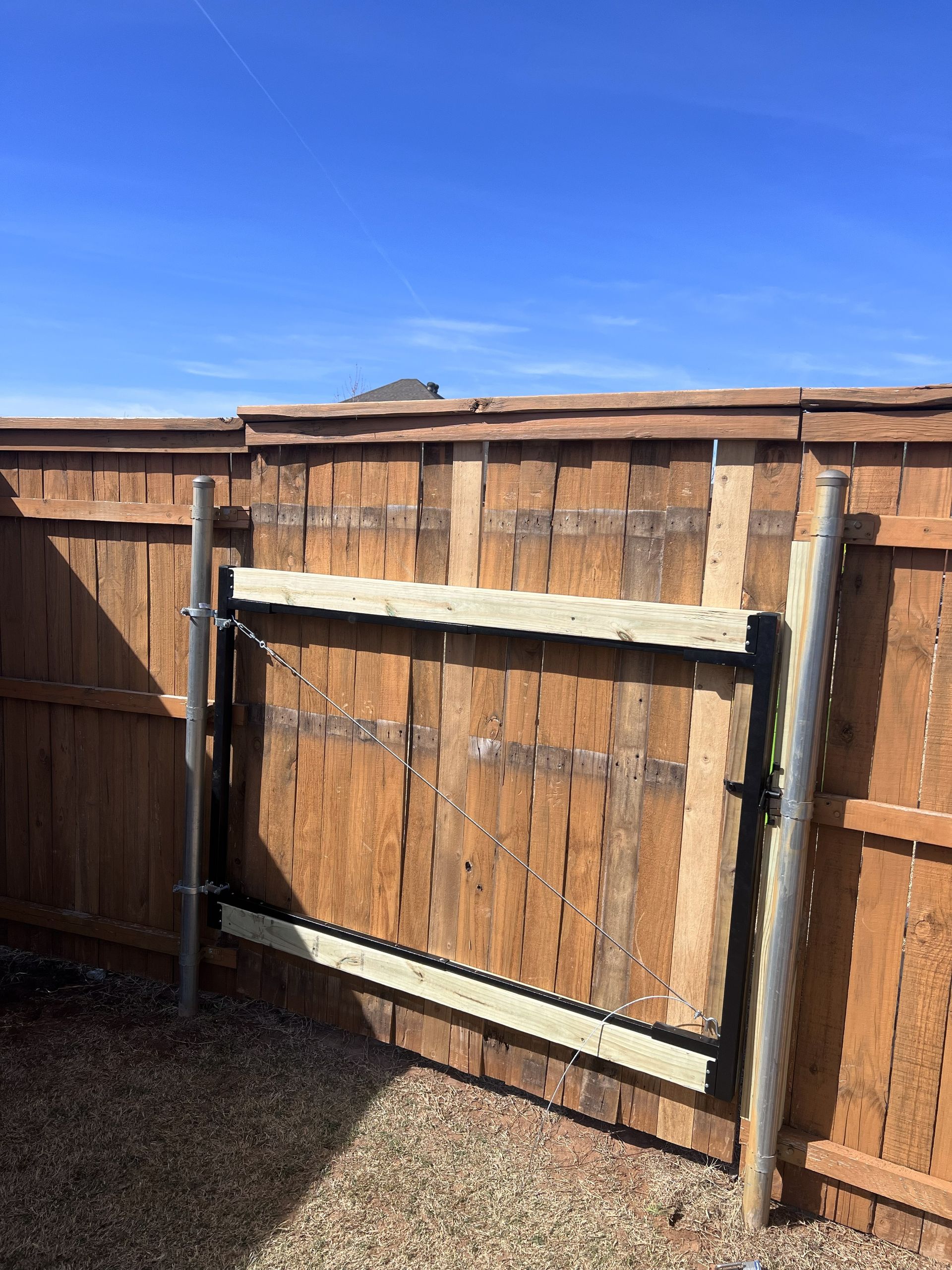 Wooden gate in a brown fence, with gravel ground and a blue sky.
