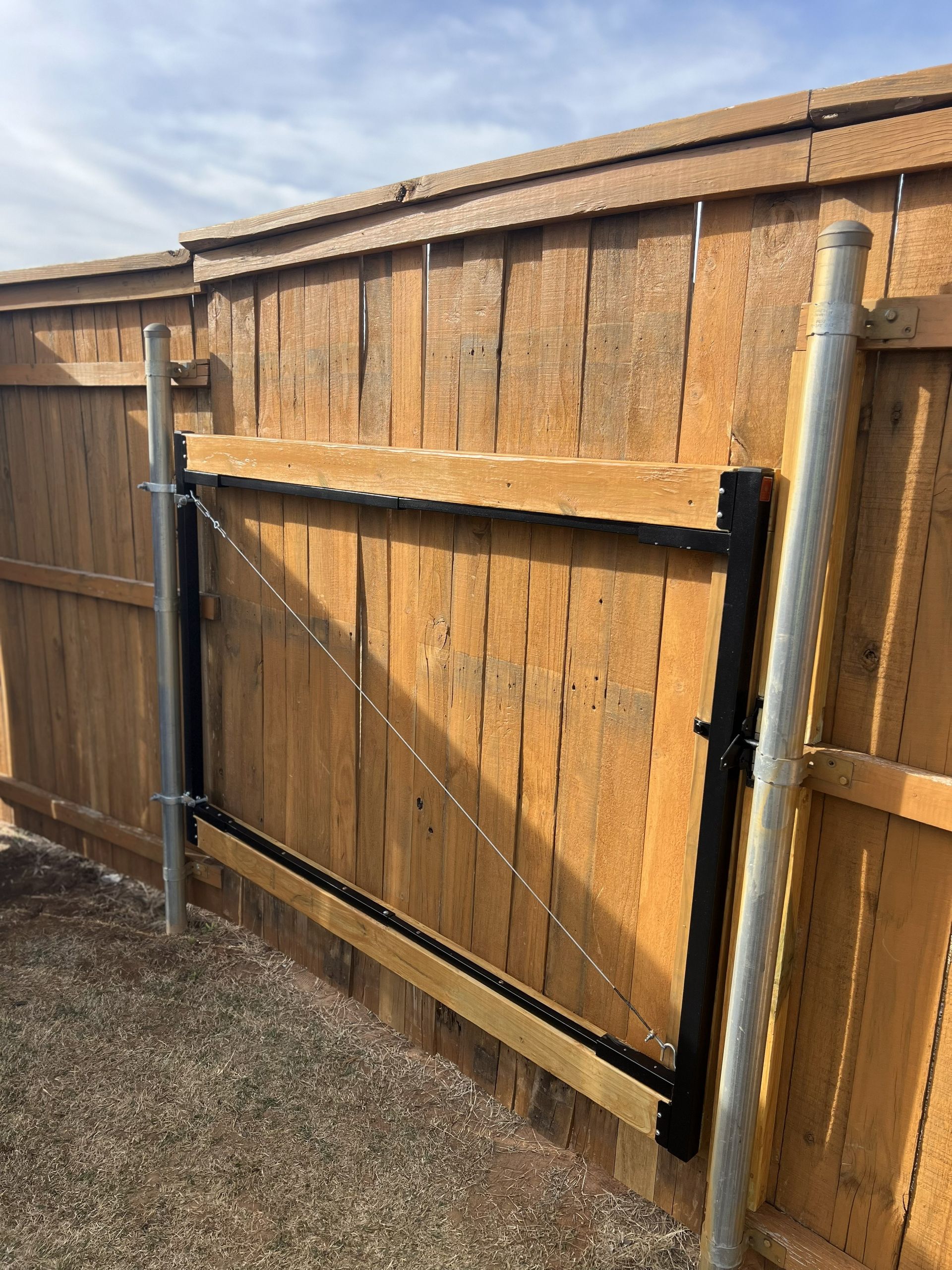 Wooden fence with a black metal gate, gravel ground.