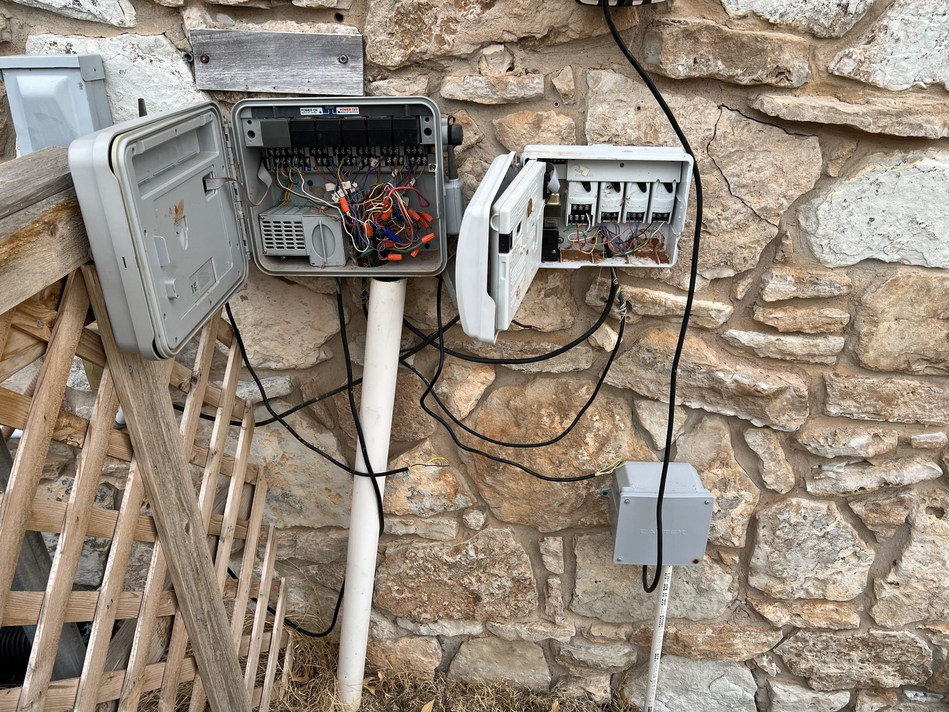 Electrical boxes and wires mounted on a stone wall.