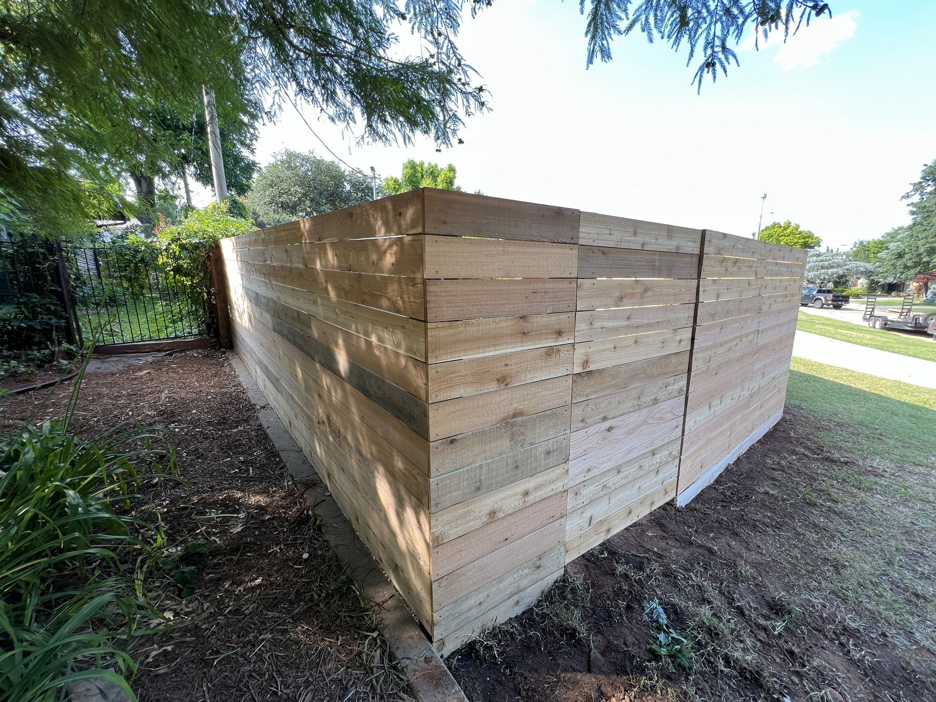 Wooden fence in a yard with trees, partially built, and bordering a sidewalk and grass.