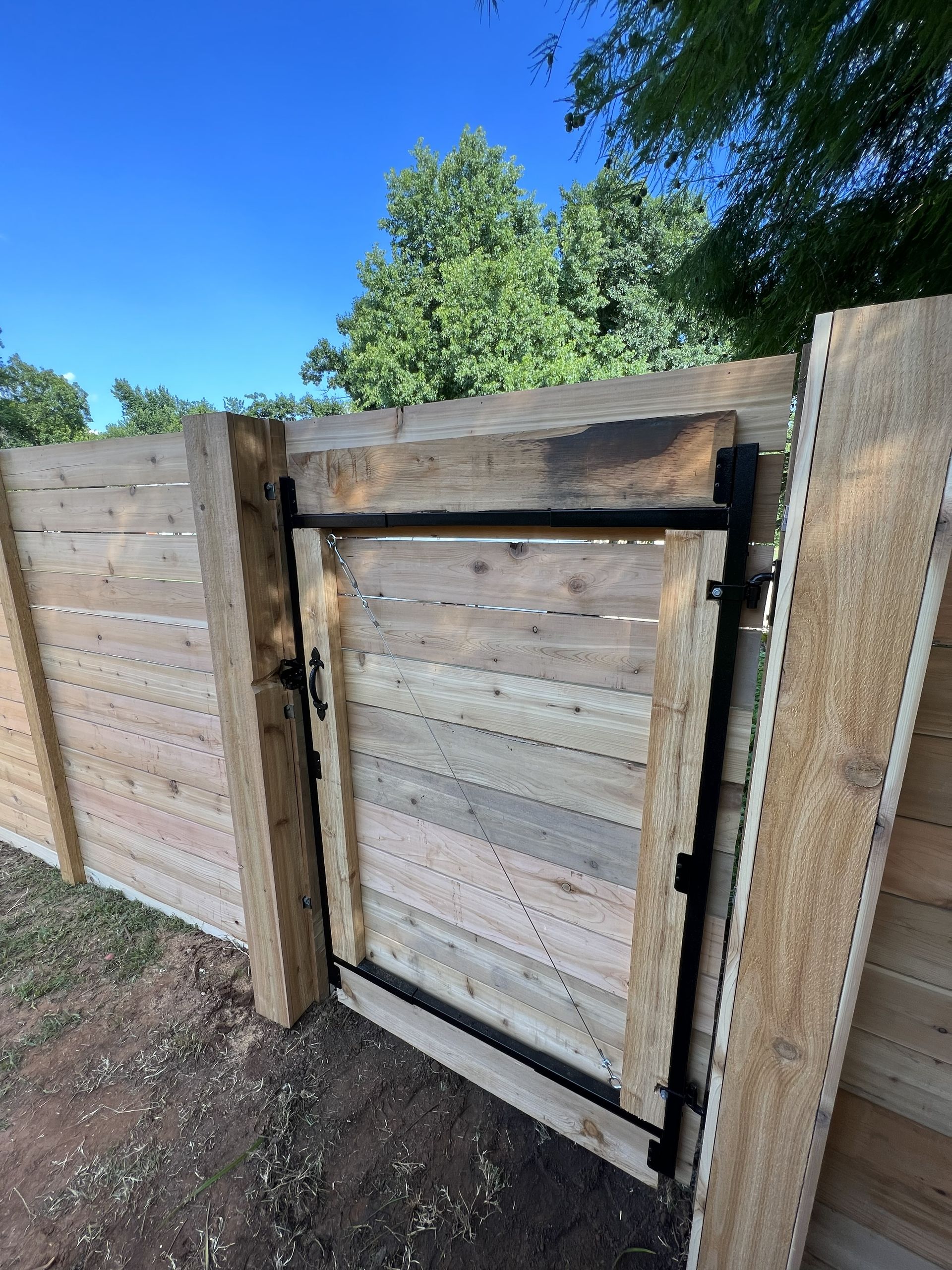 Wooden fence with gate, against a blue sky, framing a yard.